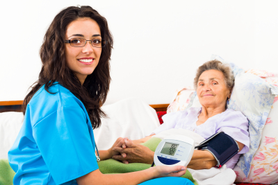 Kind nurse measuring elderly patient's blood pressure at home.