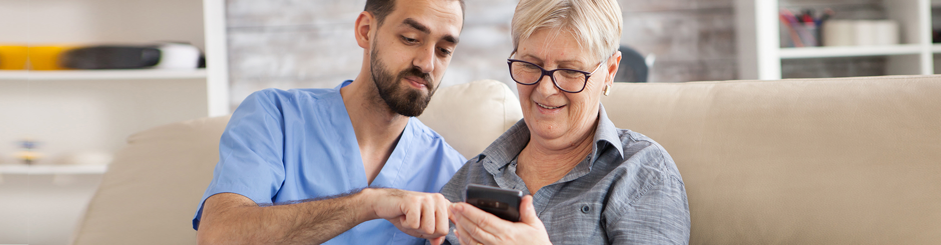 caretaker helping elder lady with phone